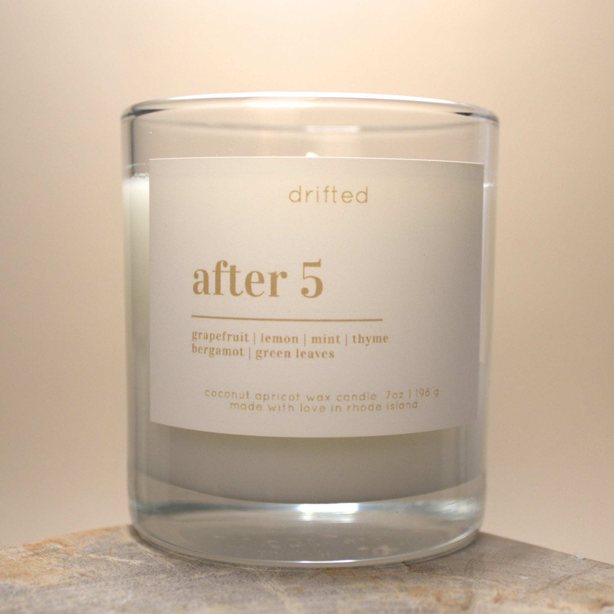 Candle in a glass jar with a label that reads 'after 5' on a neutral background