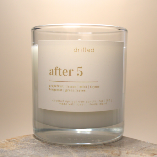 Candle in a glass jar with a label that reads 'after 5' on a neutral background