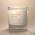 Candle in a glass jar labeled 'drifted bourbon street' on a stone surface.