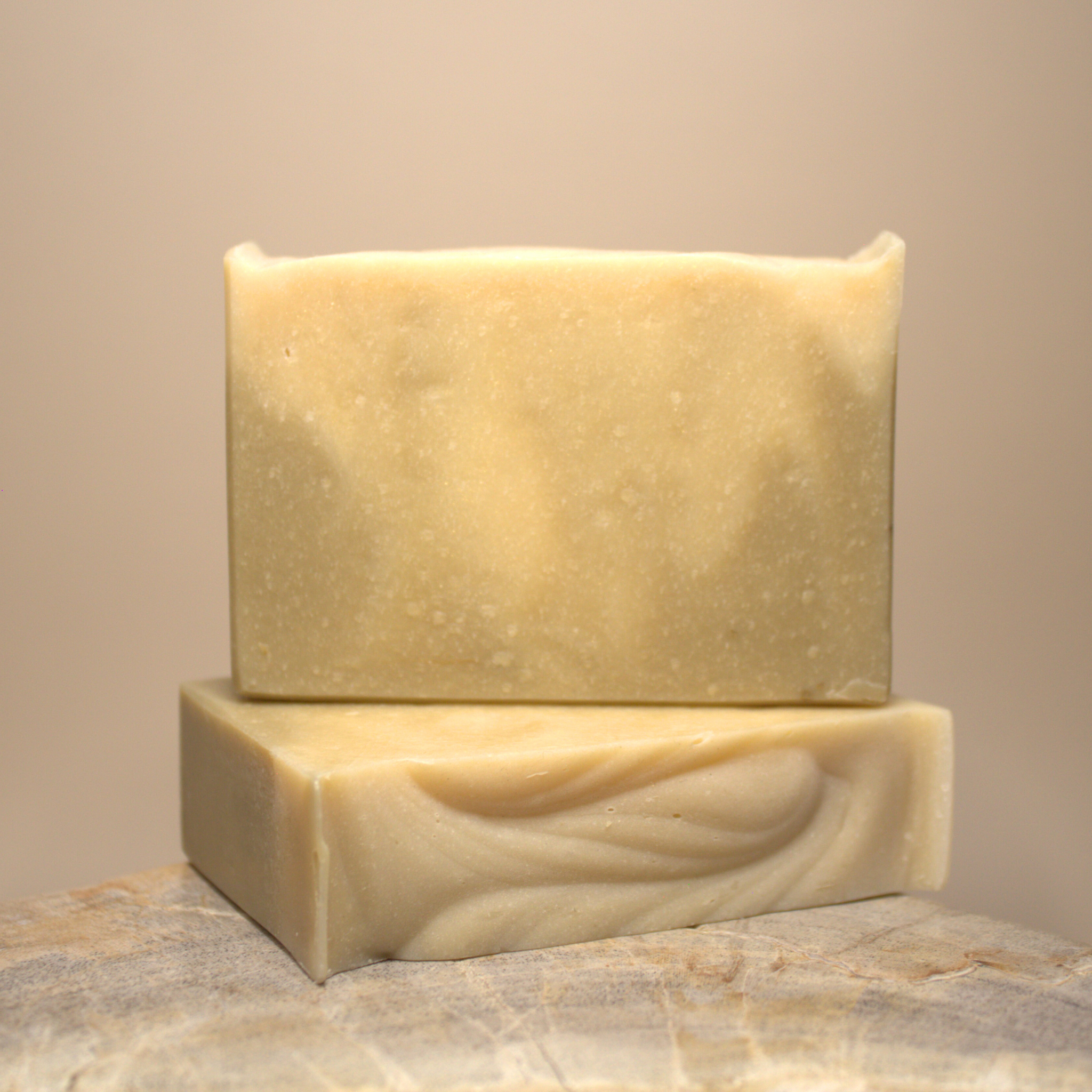 Two bars of soap on a stone surface with a neutral background