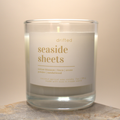 Candle with a label reading 'drifted seaside sheets' on a neutral background