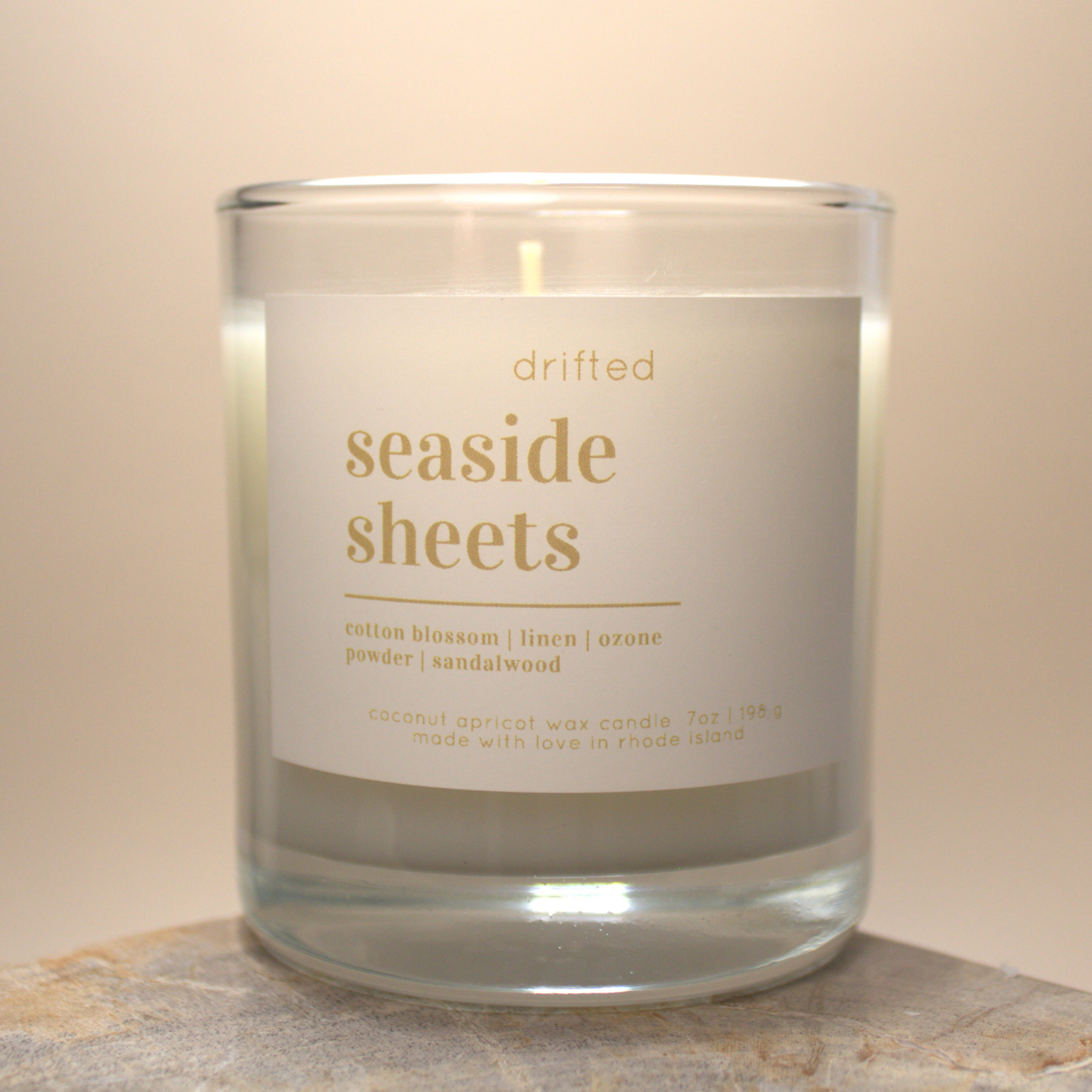 Candle with a label reading 'drifted seaside sheets' on a neutral background