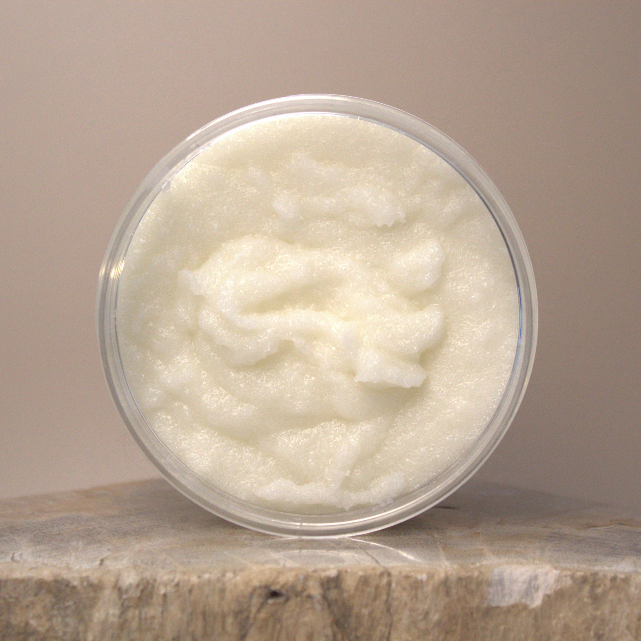 Jar of white body scrub on a stone surface with a beige background